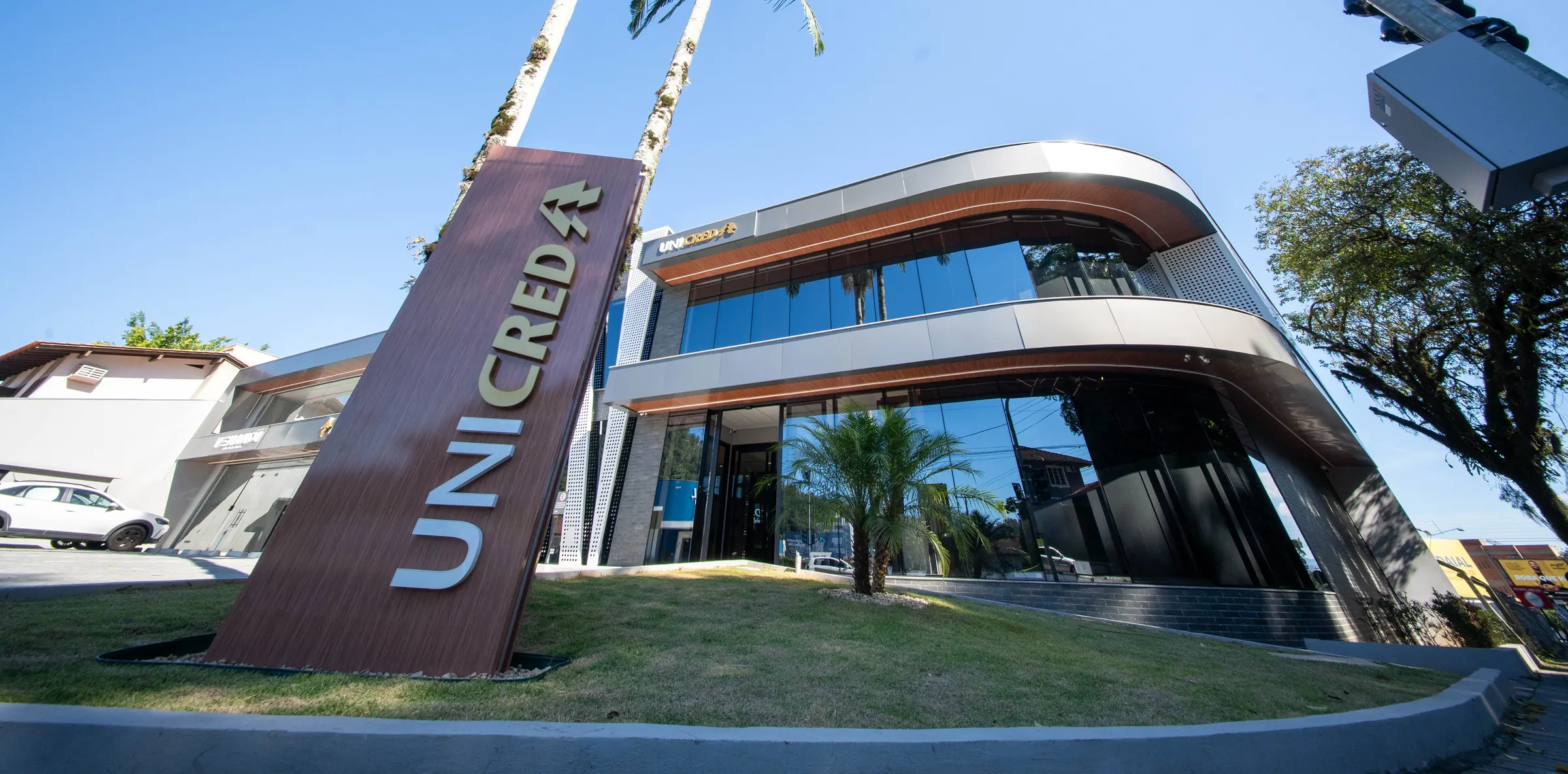 Fachada curva da agência Unicred entregue pela RAK Engenharia, com brise de madeira, vidro e letreiro da marca