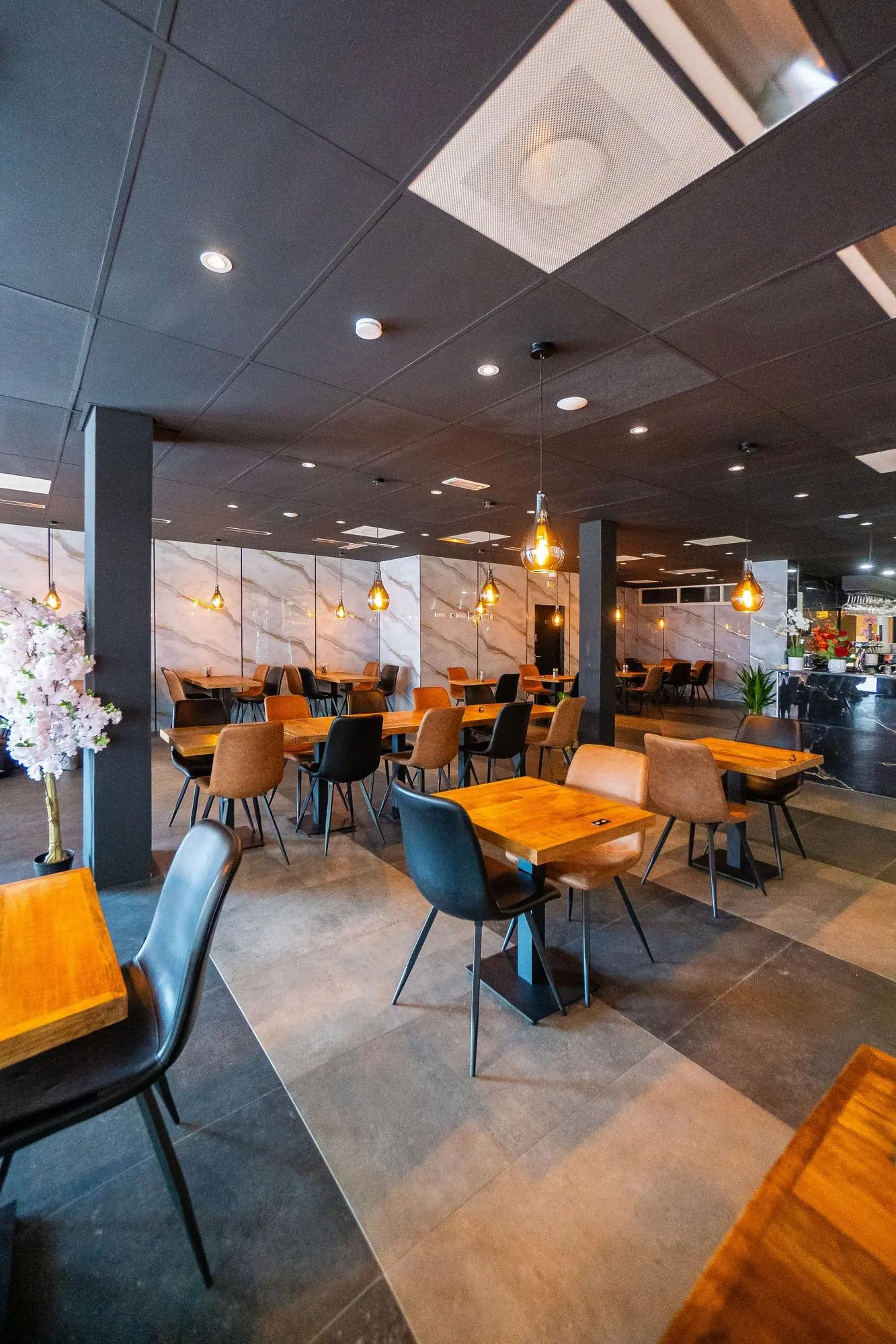 Salão de restaurante entregue, com mesas de madeira, cadeiras estofadas e iluminação pendente