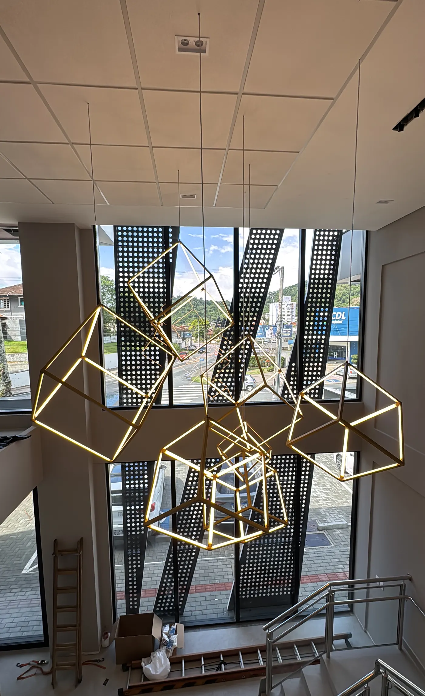 Luminárias geométricas suspensas sobre fachada envidraçada com brise metálico, obra corporativa conduzida pela RAK